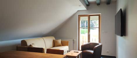 A spacious living room with a wooden dining table, a sofa, a chair, and a television mounted on the wall.