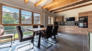 A modern kitchen with a dining area, large windows, and wooden beams.