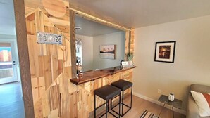 A wooden bar area with a license plate, two black stools, a small table, and a couch with a cushion.