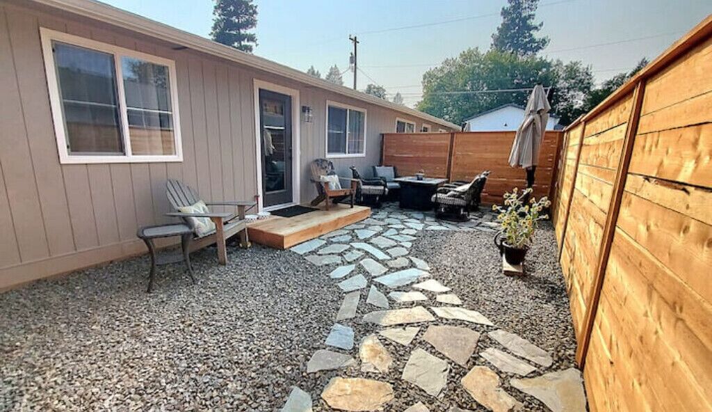 A single-story house with a patio area featuring a stone pathway, outdoor furniture, and a wooden fence.