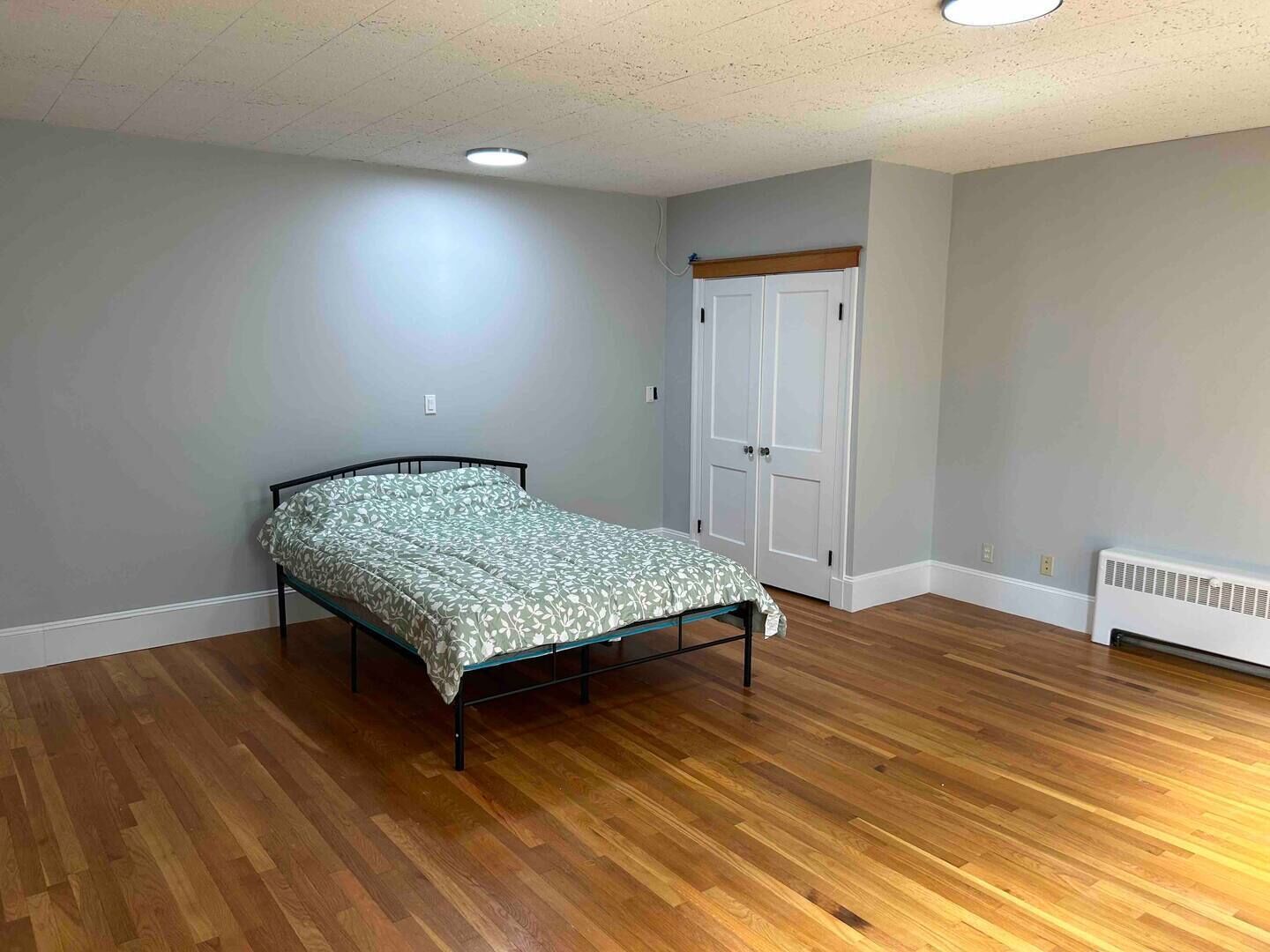 A bedroom with a bed, wooden flooring, a white radiator, and a white door.