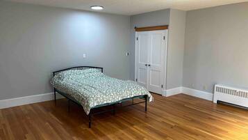 A bedroom with a bed, wooden flooring, a white radiator, and a white door.