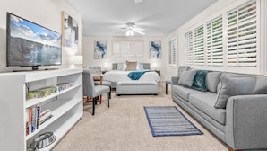 A modern living room with a TV, bookshelf, grey sofa, and a ceiling fan. - House + 2 Studios- 3 blocks from the Plaza! (Ashland)