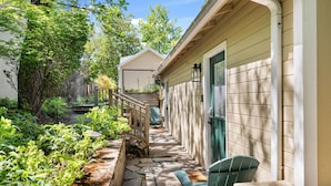 A covered outdoor area with a stone pathway, a wooden railing, and a green chair. - House + 2 Studios- 3 blocks from the Plaza! (Ashland)