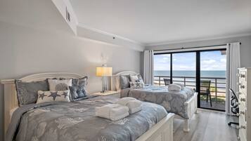 Habitación de hotel con dos camas, un balcón con vistas al mar y un aparador con cajones.