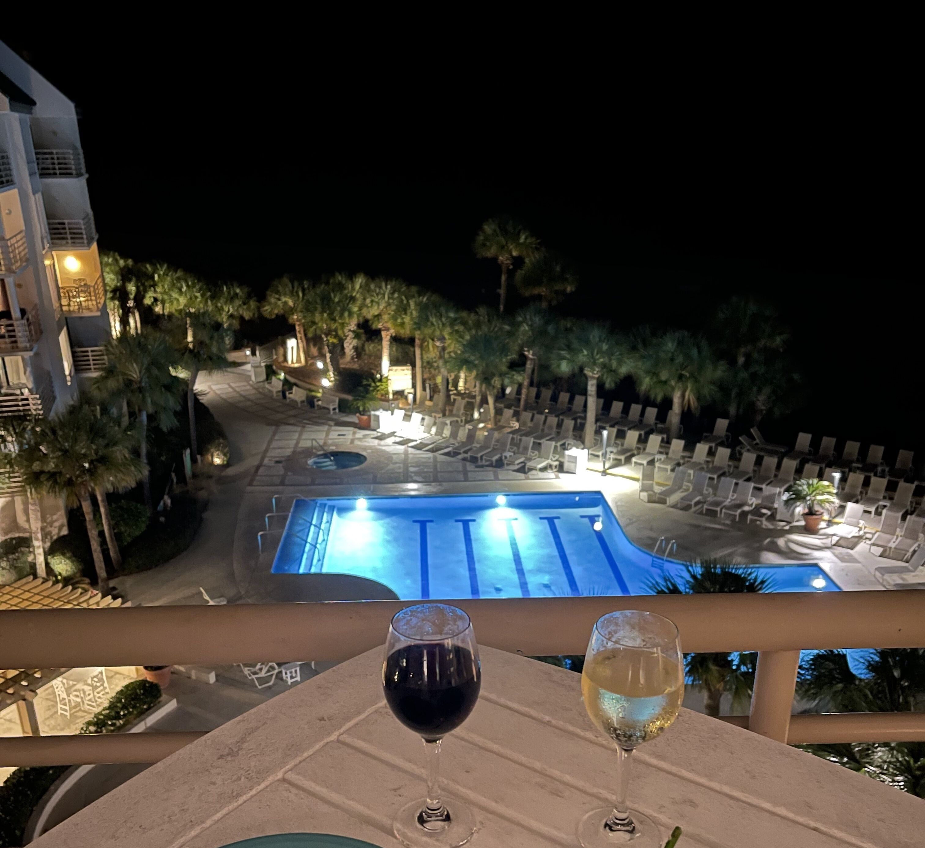 Vista nocturna de un área de piscina de hotel con sillones de descanso y una alberca.