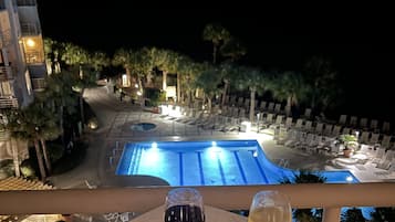Vista nocturna de un área de piscina de hotel con sillones de descanso y una alberca.
