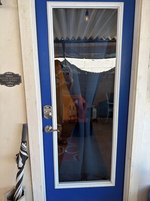 Una puerta azul con un panel de vidrio, un candado con teclado numérico y un letrero que dice 'Welcome Please Remove Your Shoes'.