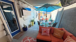 Un patio con un sofá, una mesa pequeña y un televisor montado en la pared.