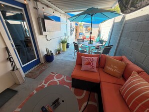 Un patio con un sofá, una mesa pequeña y un televisor montado en la pared.
