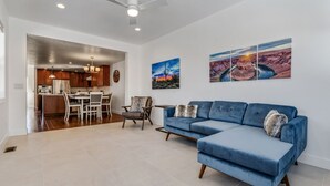 A modern living room with a blue sectional sofa, a dining area with a table and chairs, and a kitchen in the background.