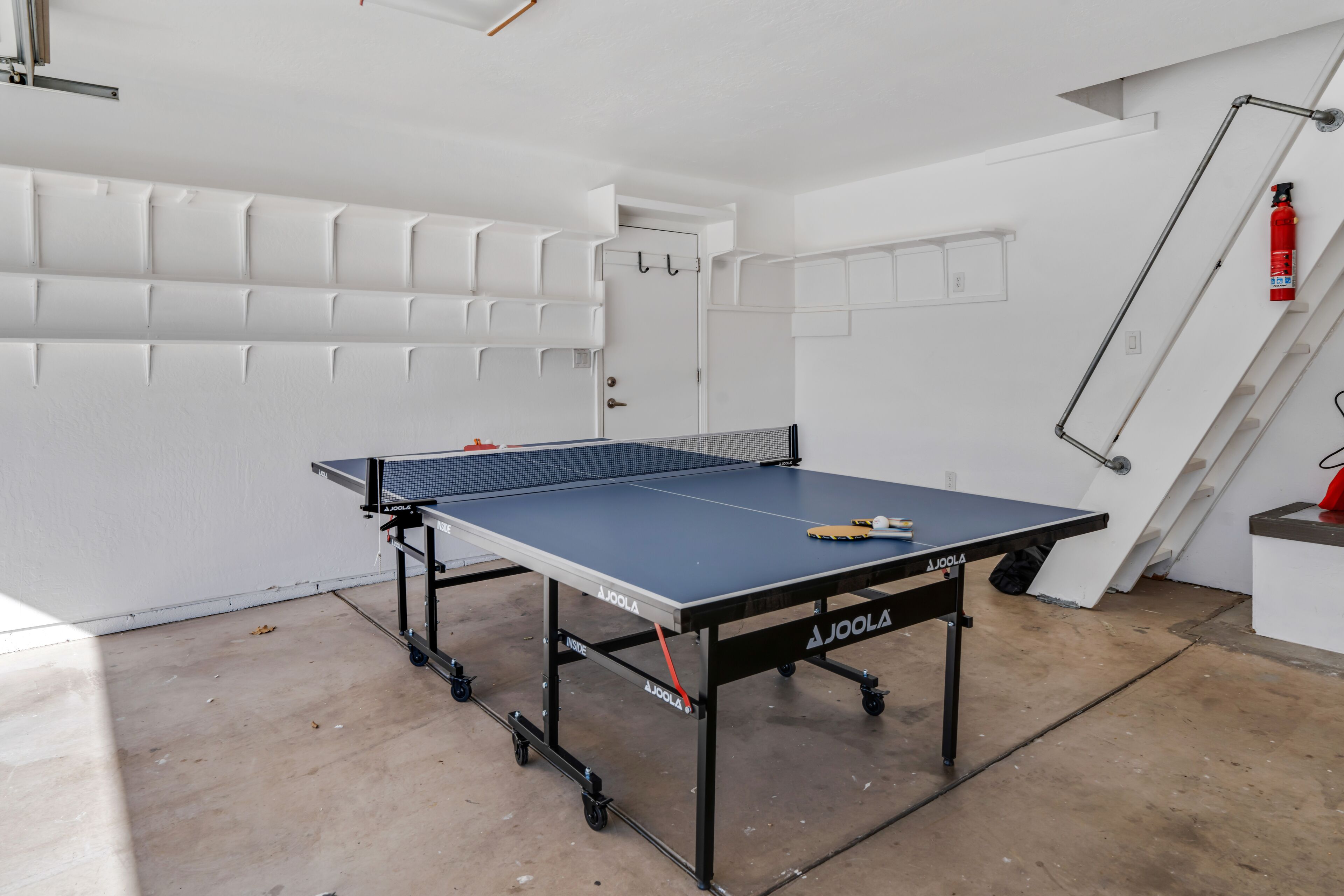 Une table de ping-pong dans une pièce aux murs blancs, avec une porte.