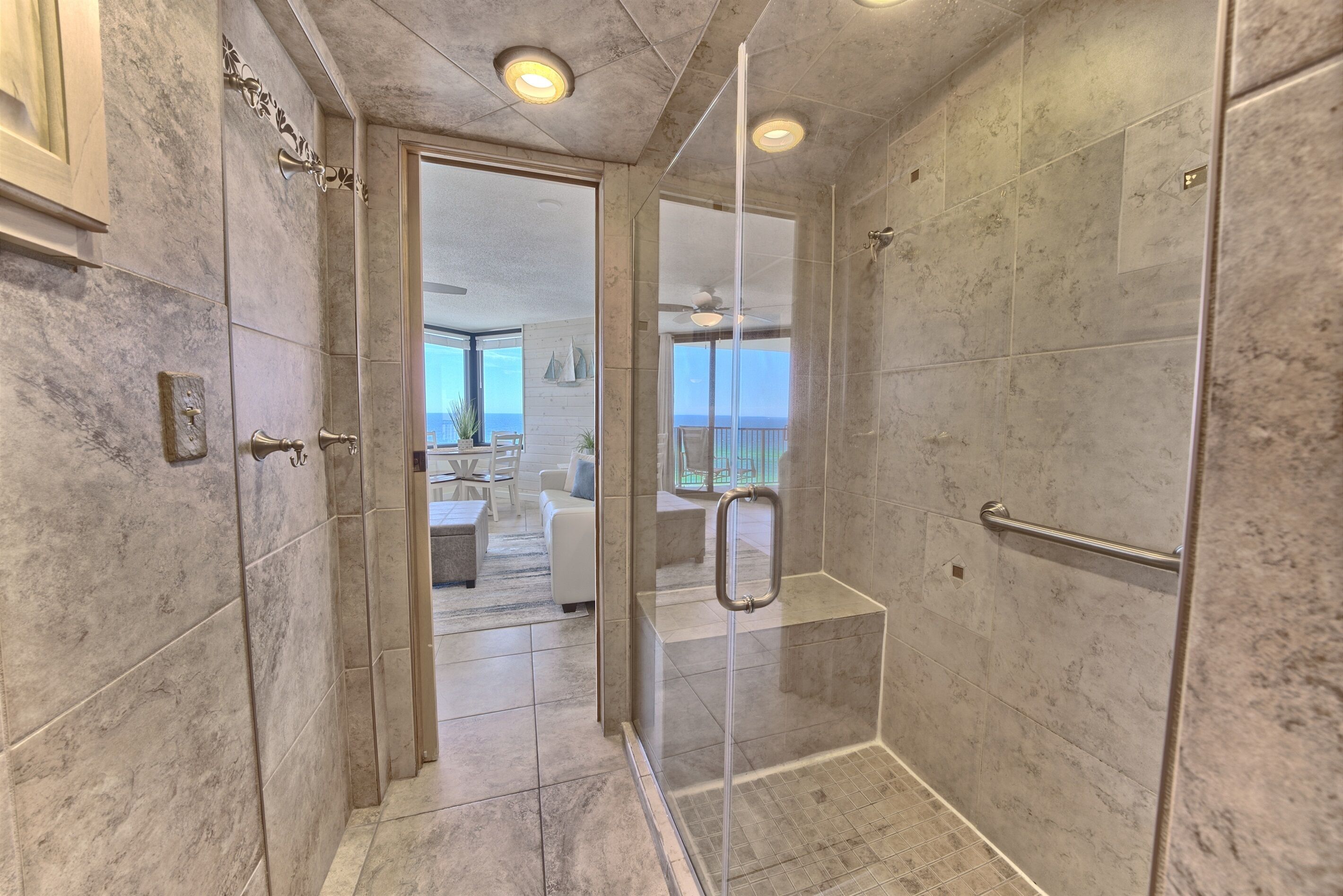 A modern bathroom with marble tiles, a glass-enclosed shower, and a view of a balcony.