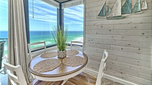 Ein runder Tisch mit Tischsets, einem Blumentopf und Blick auf das Meer durch große Fenster.