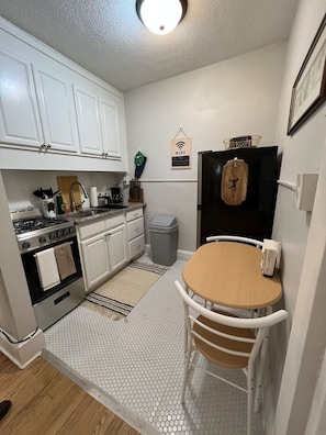 Une cuisine compacte avec des meubles blancs, une cuisinière, un évier et une petite table à manger avec des chaises.