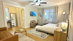 A hotel room with a bed, a desk, a chair, a TV, and a ceiling fan.