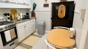 A compact kitchen with white cabinets, a stove, a sink, and a refrigerator. There's a small table with chairs and a rug on the floor.