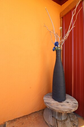 Un jarrón negro con flores azules sobre un taburete de madera frente a una pared naranja.