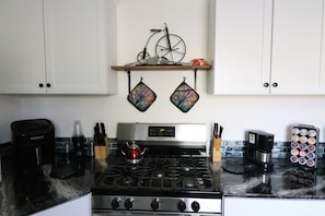 Une cuisine équipée d’une cuisinière, d’une machine à café et d’une étagère où sont posés un vélo et des objets décoratifs.