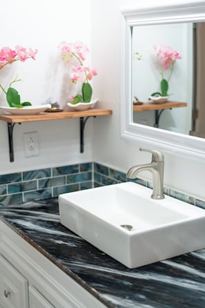 Une salle de bain avec un lavabo blanc, un miroir et des orchidées roses sur une étagère.
