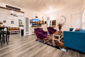 A living room with a blue sofa, purple chairs, a TV, and a ceiling fan.