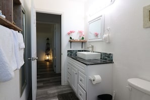 Une petite salle de bain avec un lavabo blanc, un miroir, des toilettes et une petite étagère ornée de fleurs roses.