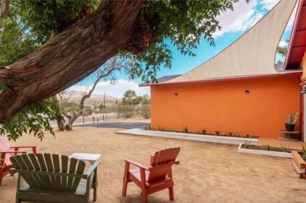 A building with an orange exterior and a sloped roof. There are two red Adirondack chairs and a green Adirondack chair in the foreground.