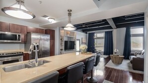 Una cocina moderna con electrodomésticos de acero inoxidable, una isla grande con taburetes de bar y un comedor con sofá y mesa de centro.