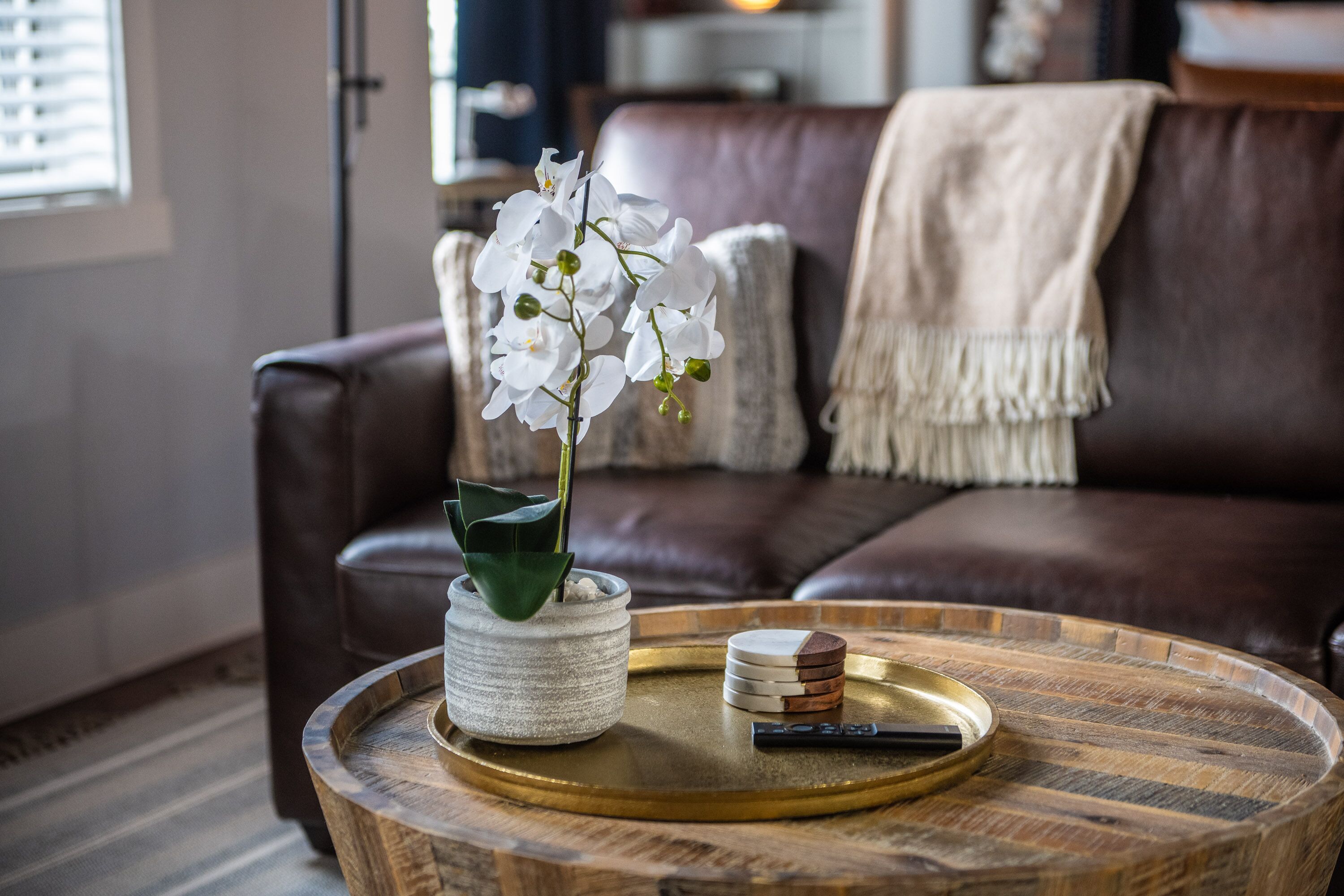 A round wooden table with a white orchid in a textured pot, a stack of coasters, and a pen.