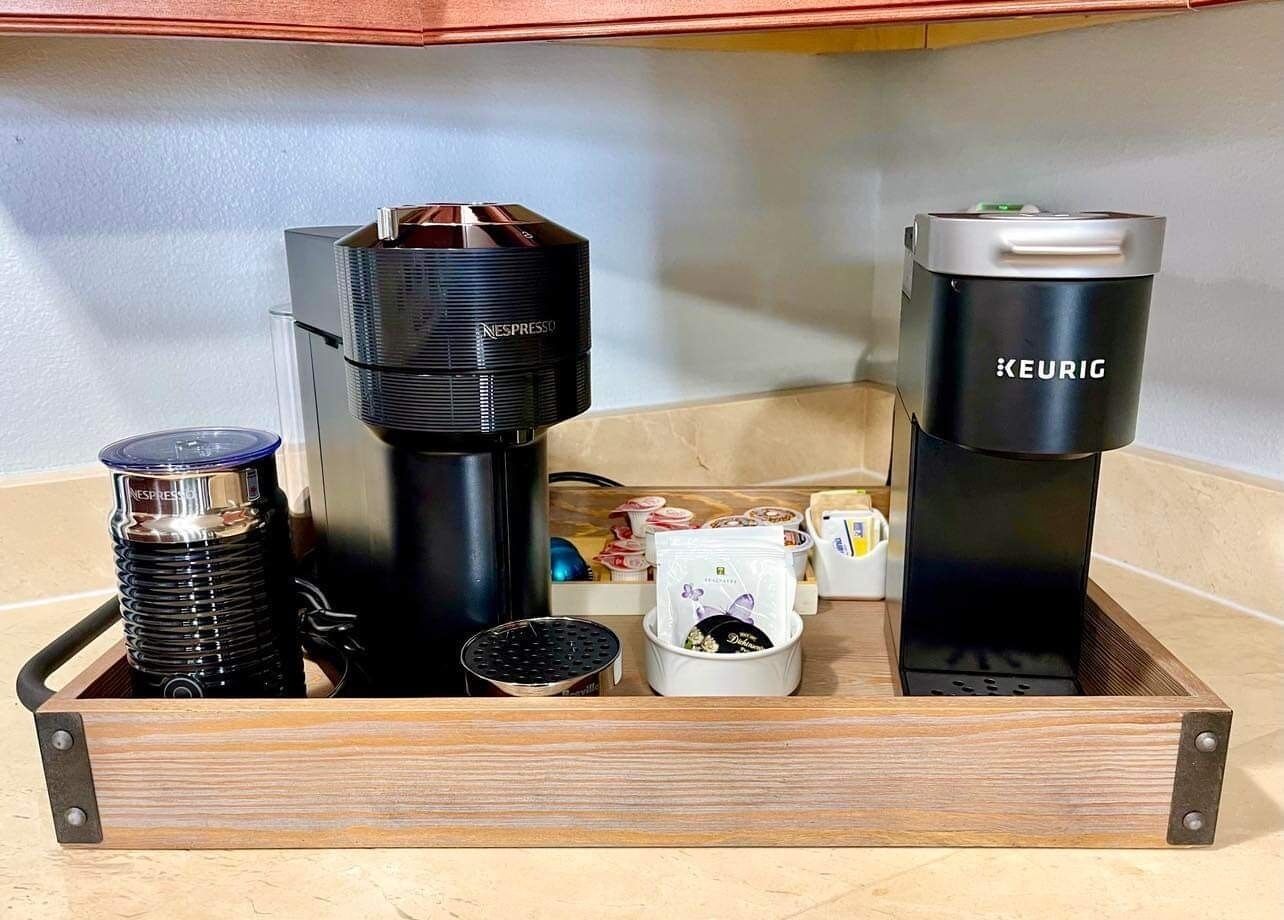 Eine Kaffeemaschine, eine Keurig-Kaffeemaschine und eine Nespresso-Maschine auf einer Holztablett.