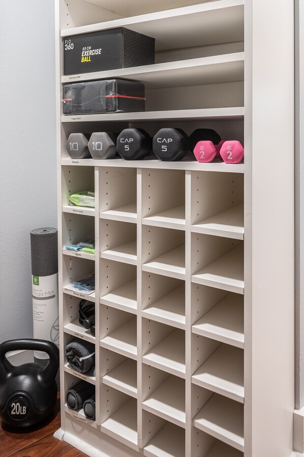 Un espacio de almacenamiento ordenado con estantes para pesas, colchonetas de yoga y otros equipos de ejercicio.