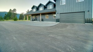 En stor bygning med to etager, garage, overdækket veranda og grusvej.