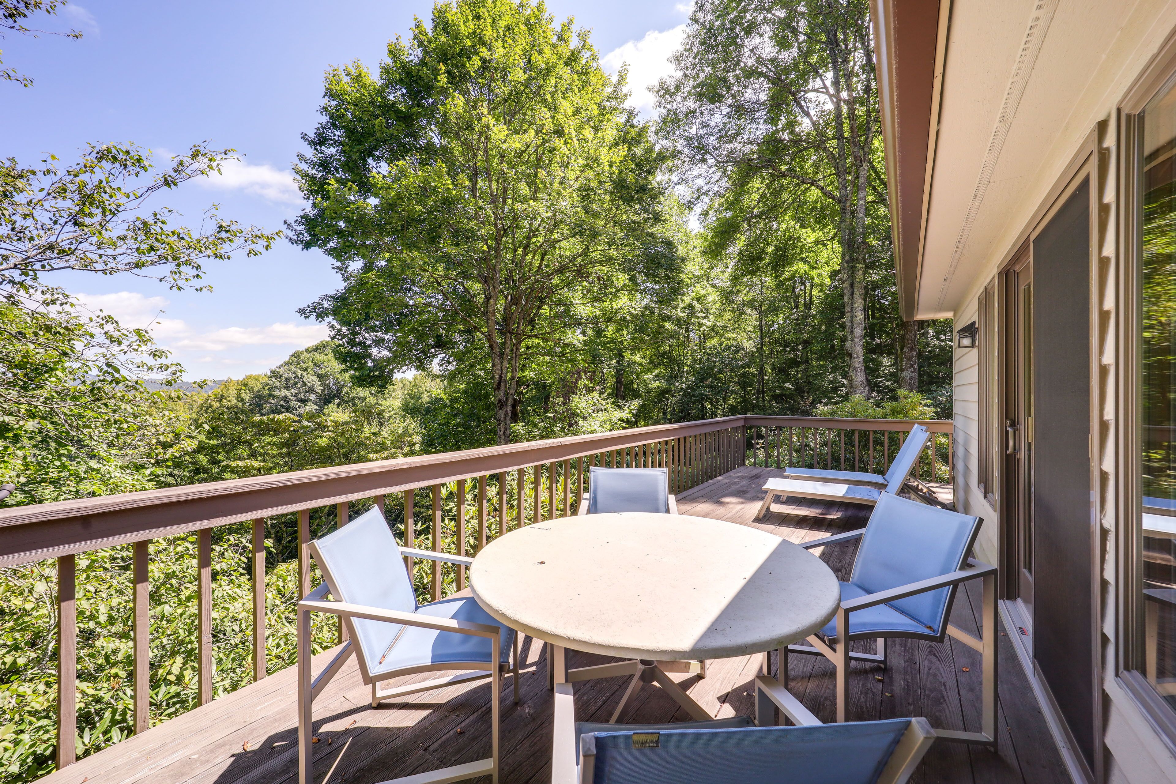 Eine Holzterrasse mit einem runden Tisch und vier Stühlen, umgeben von üppiger Vegetation und Bäumen.