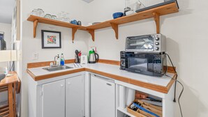 Een compacte keuken met een ingebouwde vaatwasser, een broodroosteroven en een magnetron. Daarboven staan houten planken met glazen potten en servies.