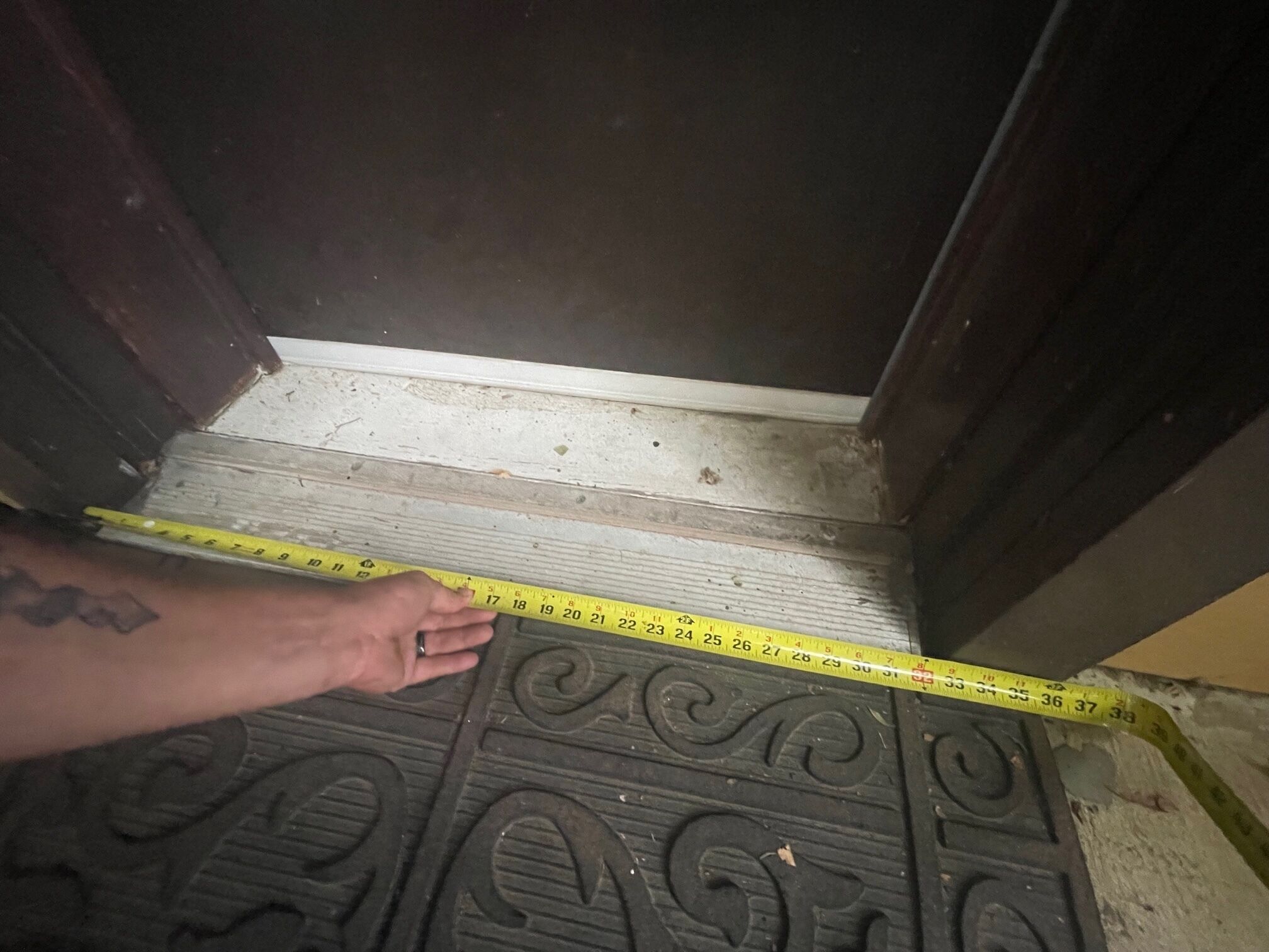 Una mano midiendo el ancho de una puerta con un metro de cinta amarilla.