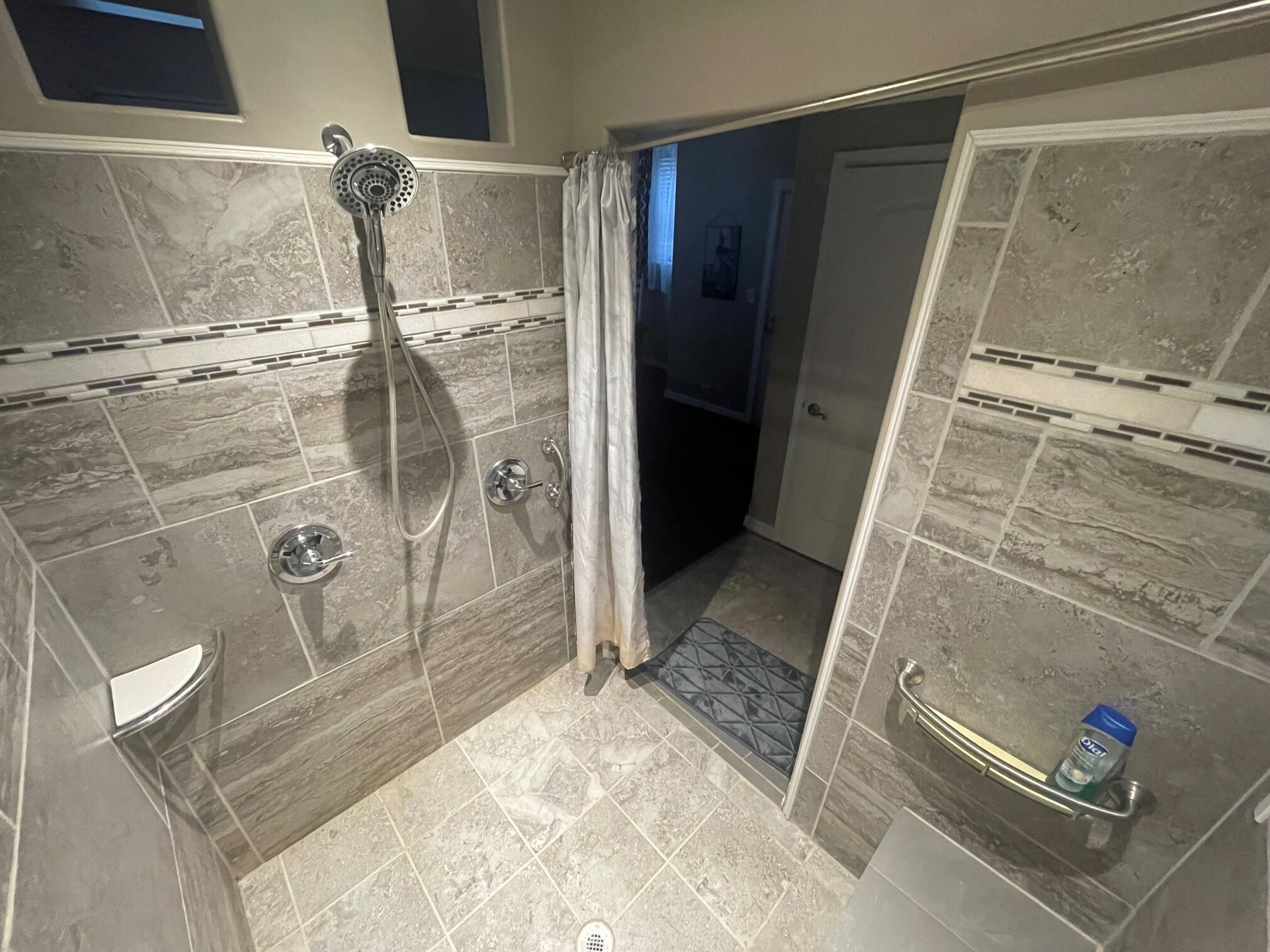 A walk-in shower with a handheld showerhead, a glass door, and a towel rack with a bottle.