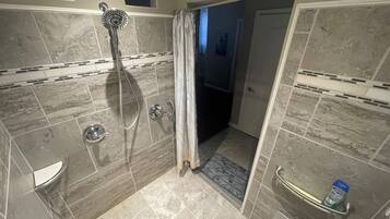 A walk-in shower with a handheld showerhead, a glass door, and a towel rack with a bottle.