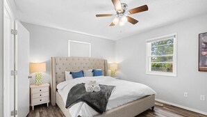 A bedroom with a bed, nightstands, a ceiling fan, a window, and a door. - Stylish Rancher in Quiet, Tree Lined Neighborhood. (Joplin)