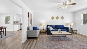A modern living room with a blue sofa, a coffee table, and a ceiling fan. - Stylish Rancher in Quiet, Tree Lined Neighborhood. (Joplin)