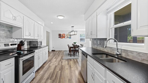 A modern kitchen with white cabinets, a black countertop, and a wooden floor. - Stylish Rancher in Quiet, Tree Lined Neighborhood. (Joplin)