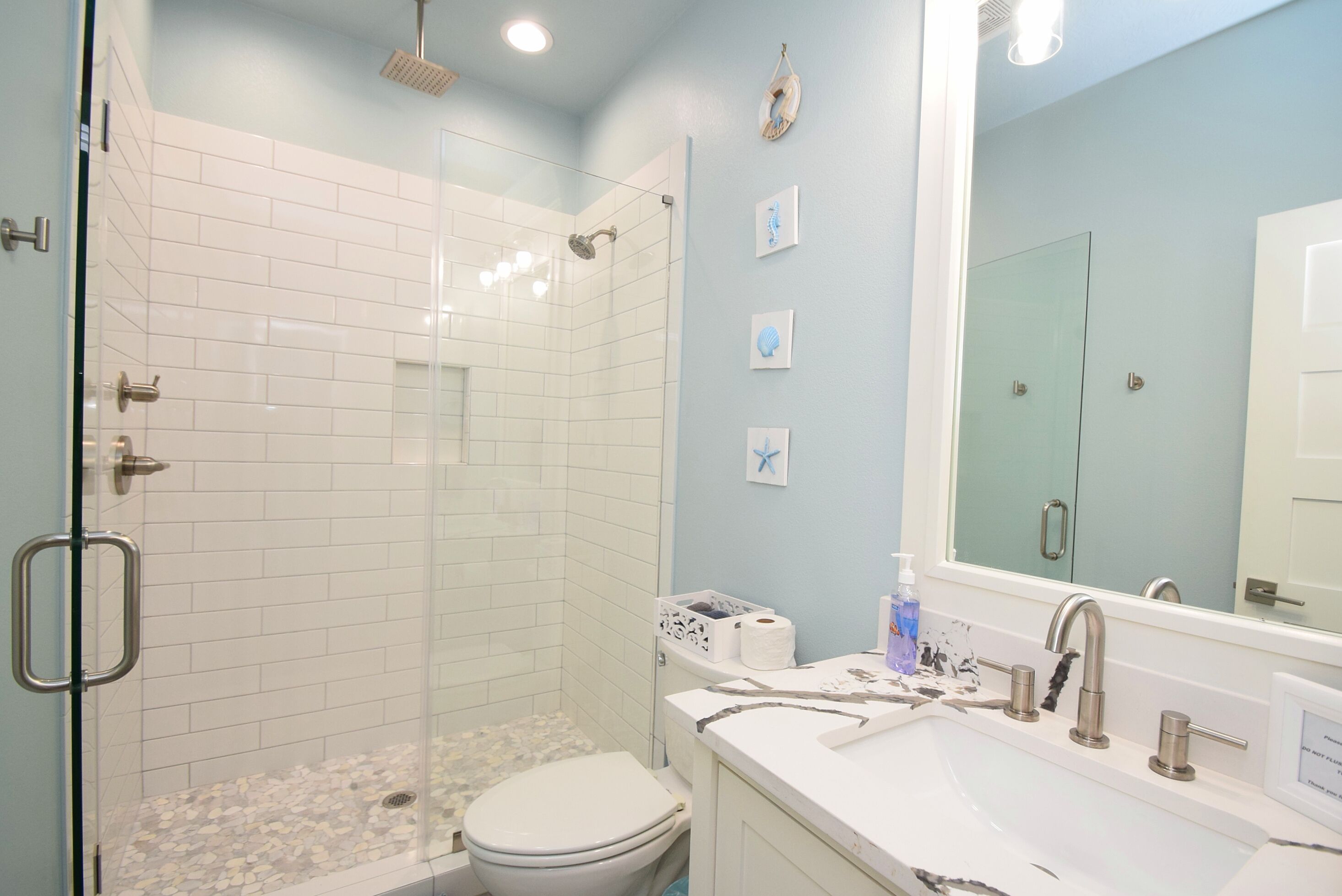 A bathroom with a glass-enclosed shower, a white toilet, and a sink with a mirror.