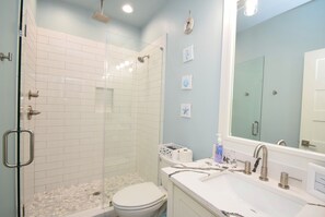 A bathroom with a glass-enclosed shower, a white toilet, and a sink with a mirror. - Beach Sands 1  (Port Bolivar)