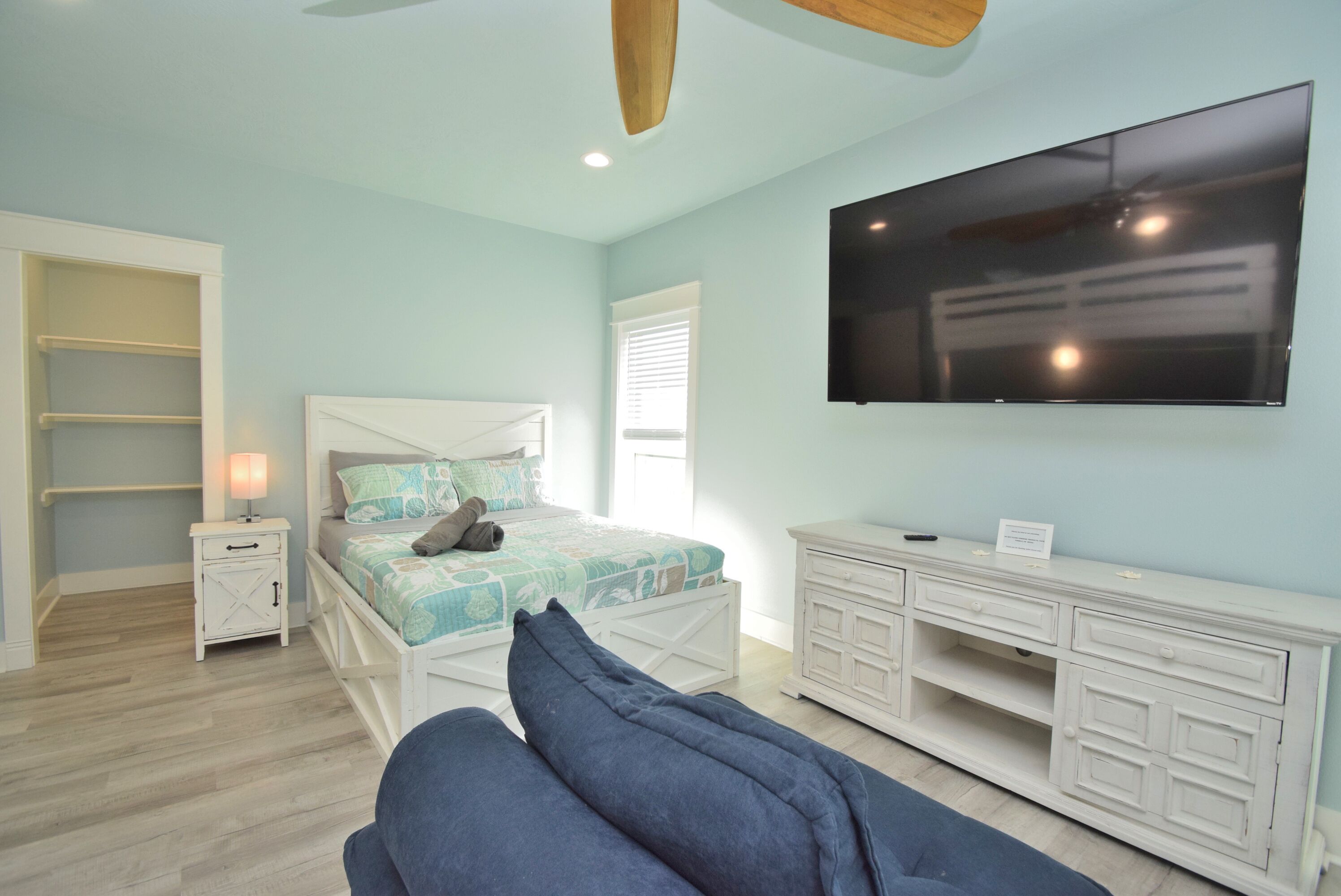 Un dormitorio con cama, televisión, mesita de noche, cómoda y ventilador de techo.