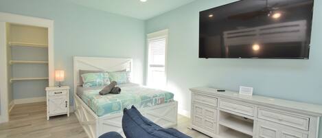 Un dormitorio con cama, televisión, mesita de noche, cómoda y ventilador de techo.