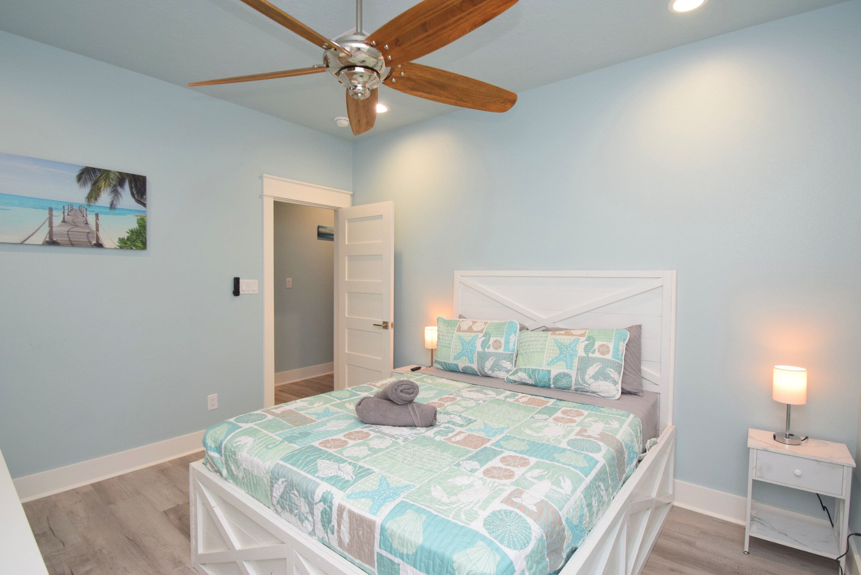 A bedroom with a bed, a ceiling fan, a nightstand, and a painting on the wall.