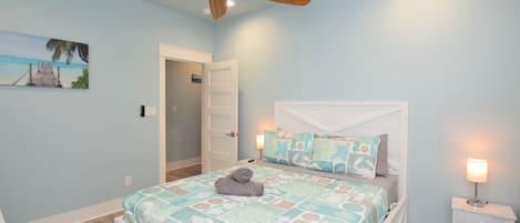A bedroom with a bed, a ceiling fan, a nightstand, and a painting on the wall.