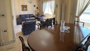 Een ruime woonkamer met een grote ronde tafel, een zithoek en een eethoek.