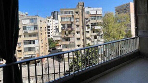 Een balkon met een metalen hekwerk met uitzicht op een stadsgezicht met hoge gebouwen.
