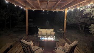 Een buitenpatio met een houten terras, een tafel met stoelen, lichtjes en een overdekt gebied met een barbecue.