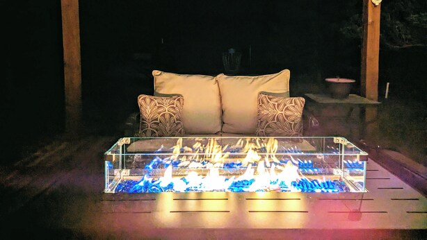 A glass-top fire feature with a sofa and patterned cushions in a dimly lit outdoor area. - Inviting & Spacious! Unique indoor and outdoor vibe! (Walsenburg)